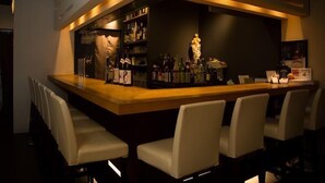 Una zona de bar con mostrador, taburetes y una variedad de botellas.