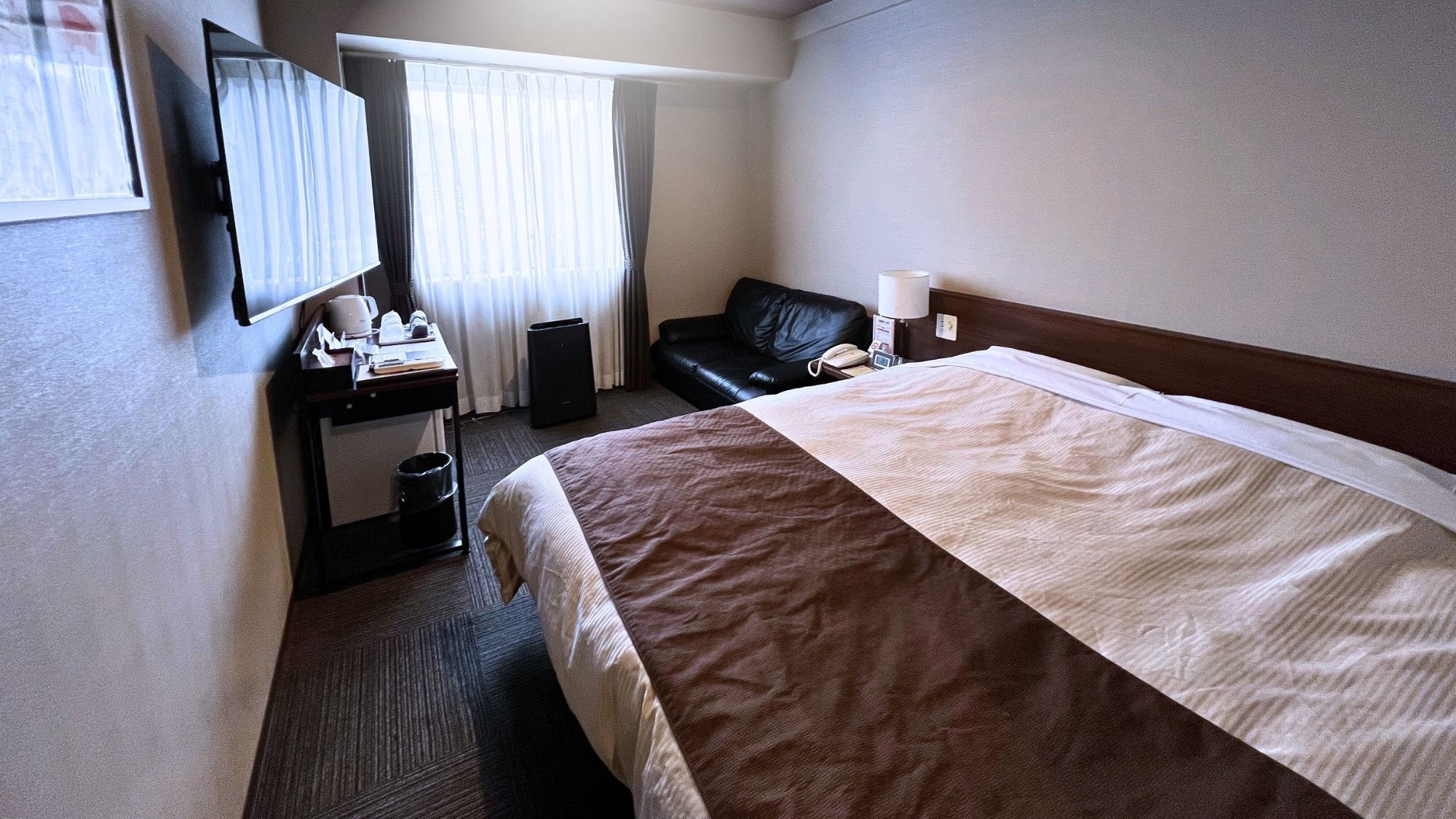 Habitació d'hotel amb llit, escriptori, cadira, televisió i finestra amb cortines.
