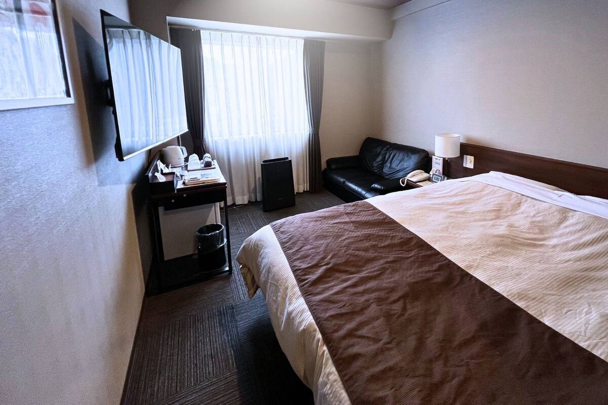 Habitación de hotel con cama, escritorio, silla, televisor y ventana con cortinas.