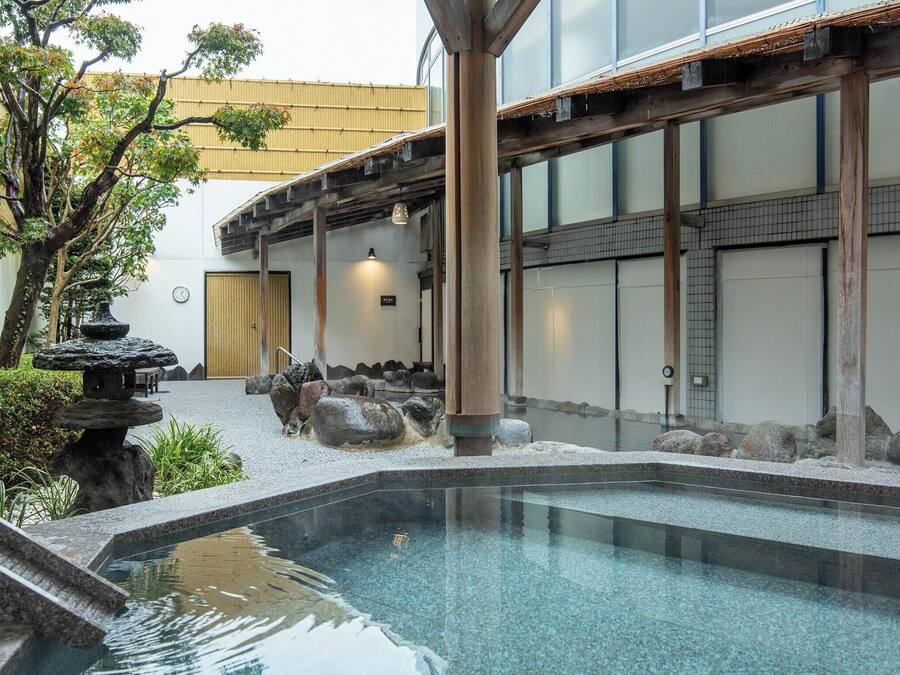 Zona de piscina de estilo japonés tradicional, con un farol de piedra, vigas de madera y vistas a un edificio con puertas correderas.