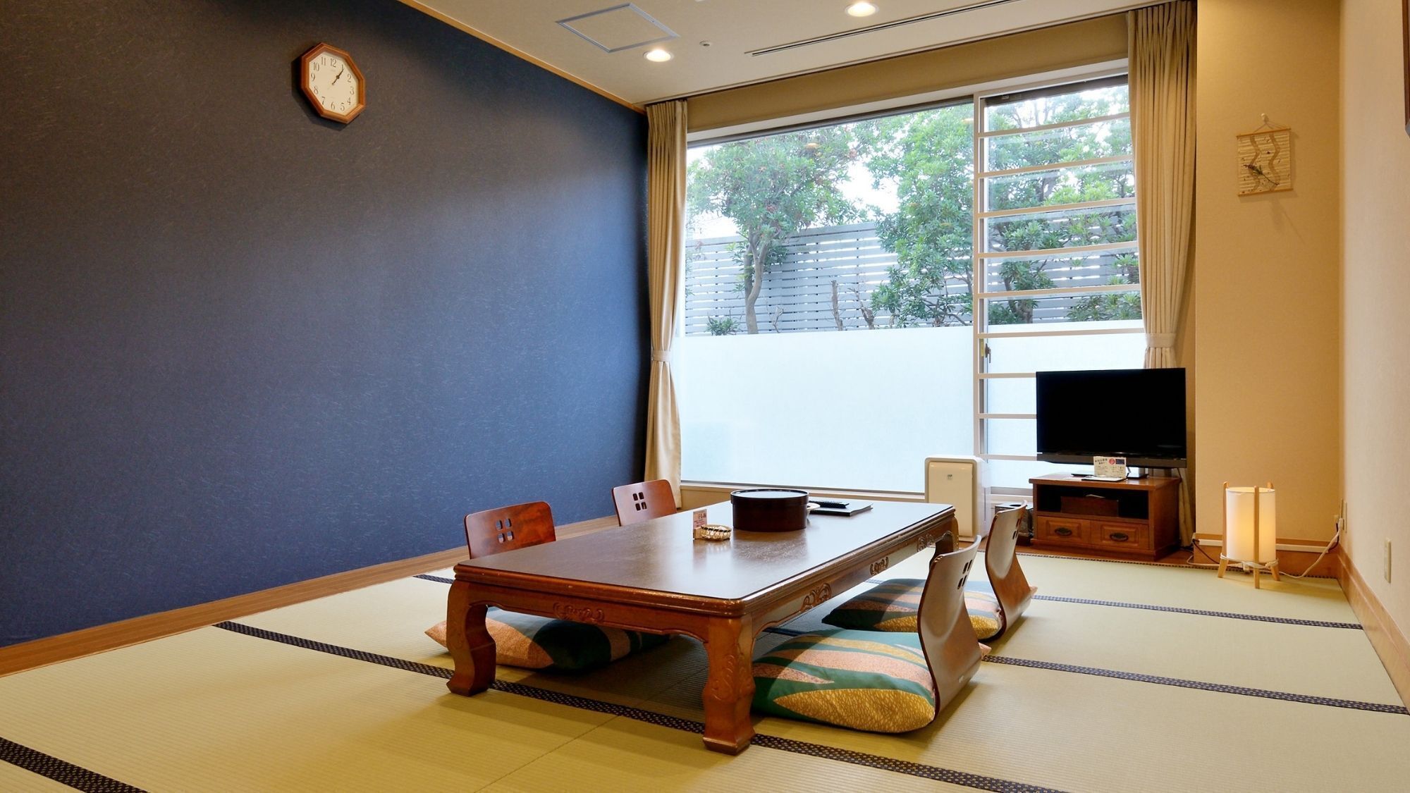 Una habitació tradicional amb tatami, taula baixa, cadires, televisió i un rellotge a la paret.