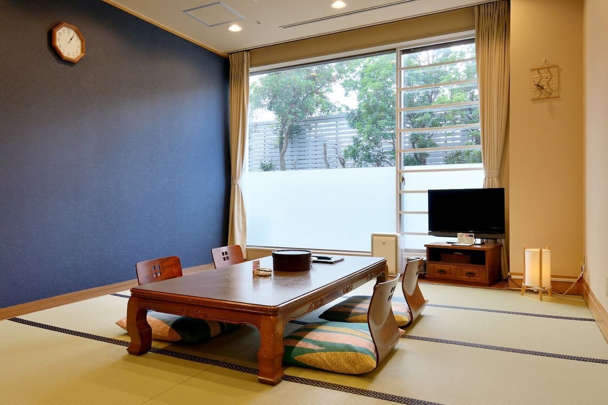 Una habitación tradicional de tatami con una mesa baja, sillas, un televisor y un reloj en la pared.