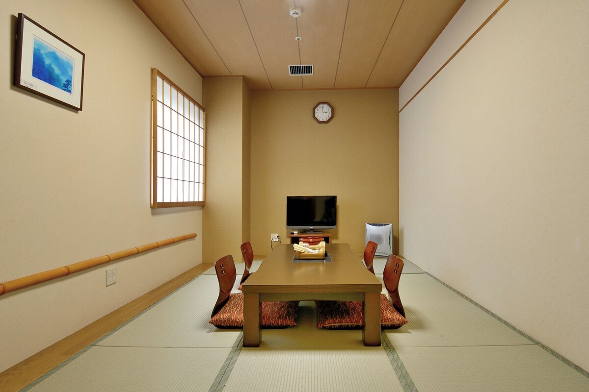 Un salón de conferencias con una mesa de madera, sillas, un televisor y un reloj en la pared.