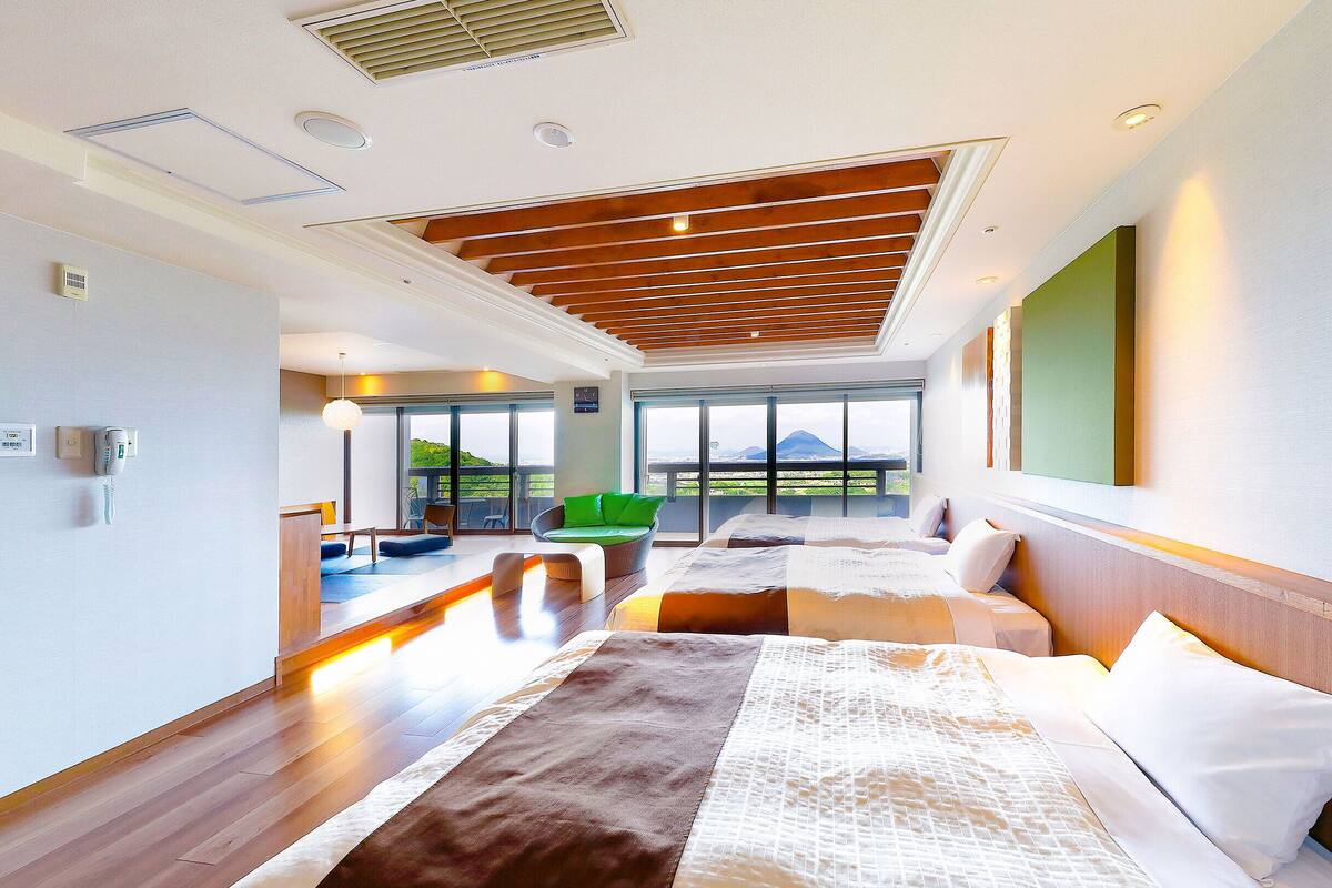 Une chambre d’hôtel moderne avec un grand lit, un fauteuil vert et une vue sur l’extérieur.