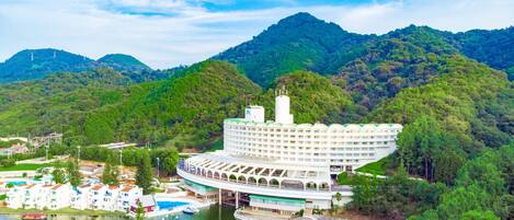 A large, white, multi-story hotel with a unique curved roof, situated by a lake with a bridge connecting to a mainland.