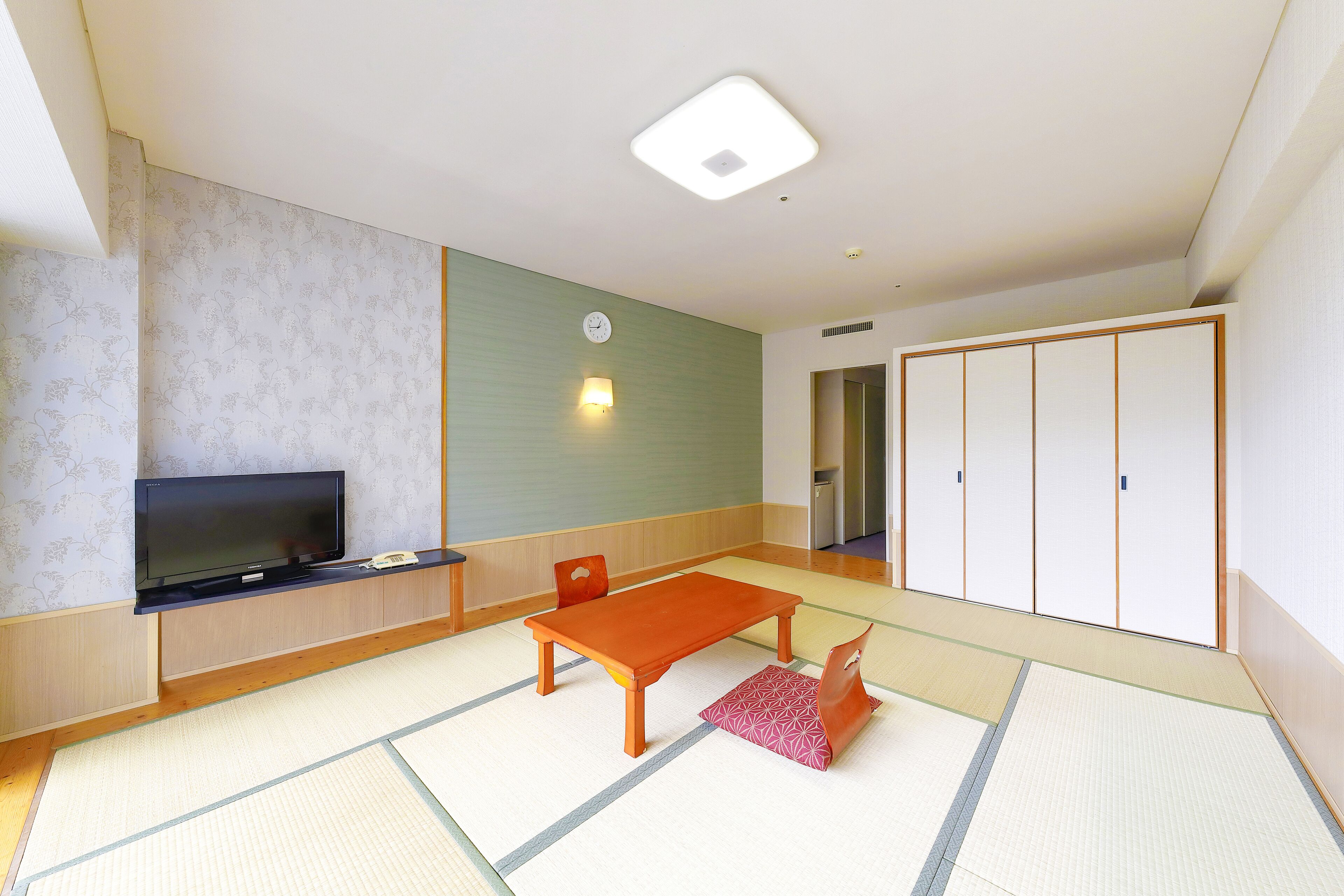 A room with tatami flooring, a television on a low stand, a wooden table, and a wardrobe with sliding doors.