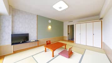 A room with tatami flooring, a television on a low stand, a wooden table, and a wardrobe with sliding doors.