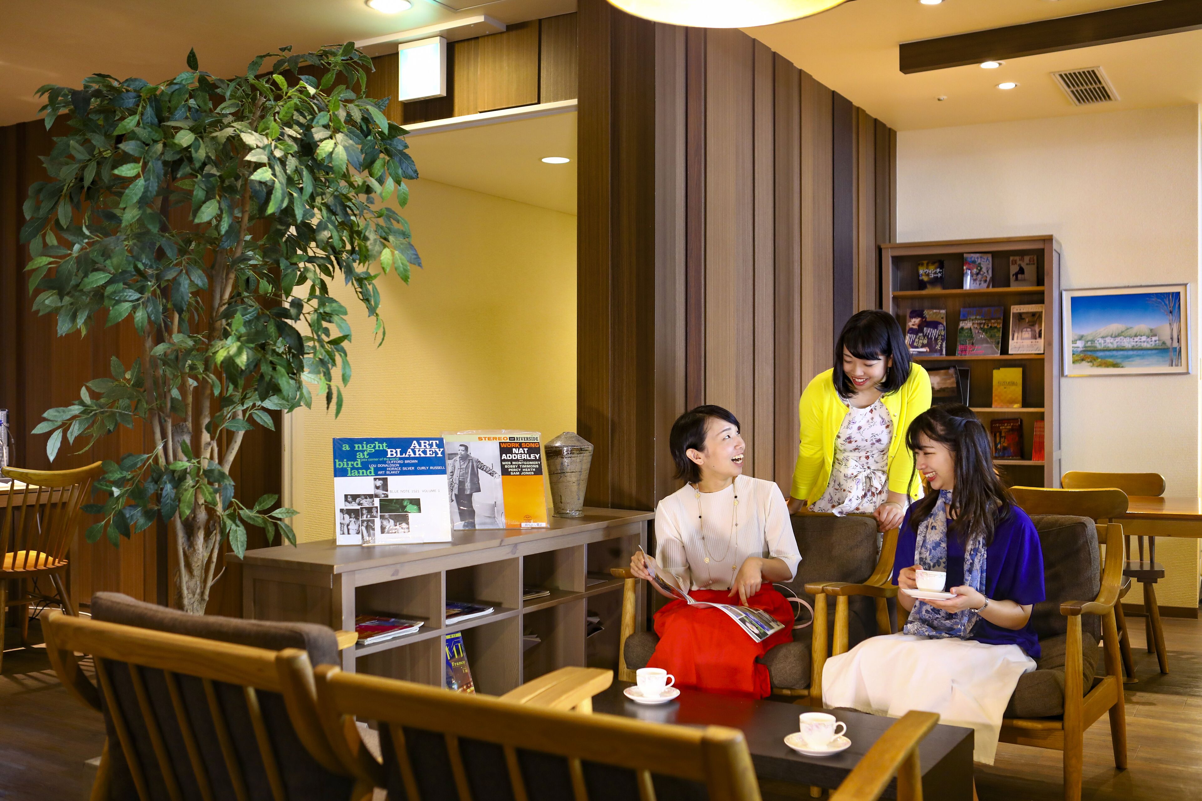 A cozy indoor seating area with wooden furniture, a large potted plant, and a bookshelf with books and magazines.