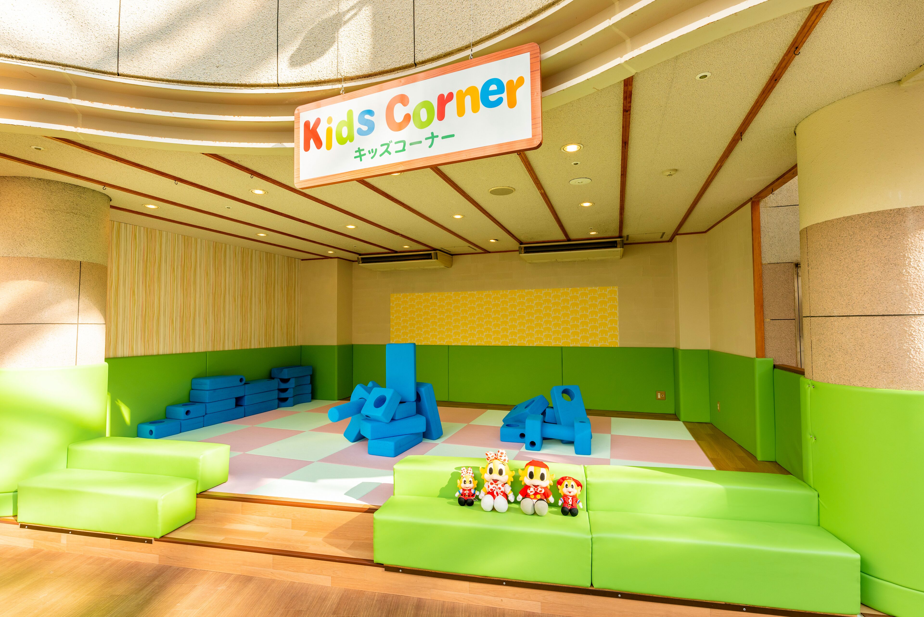 A children's play area with a sign reading "Kids Corner," featuring green seating and blue play structures.