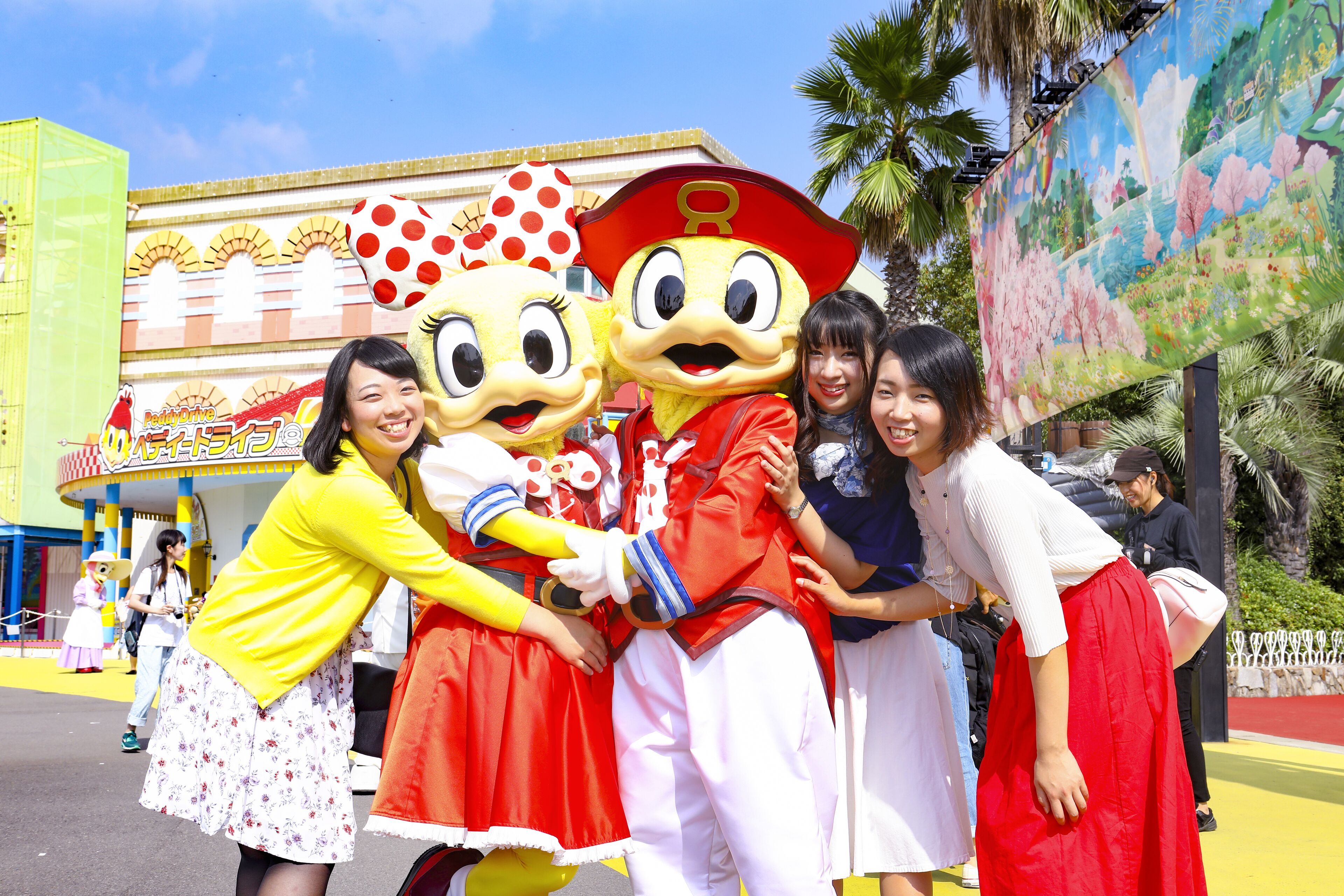 A group of people posing with two cartoon characters in front of a colorful building.