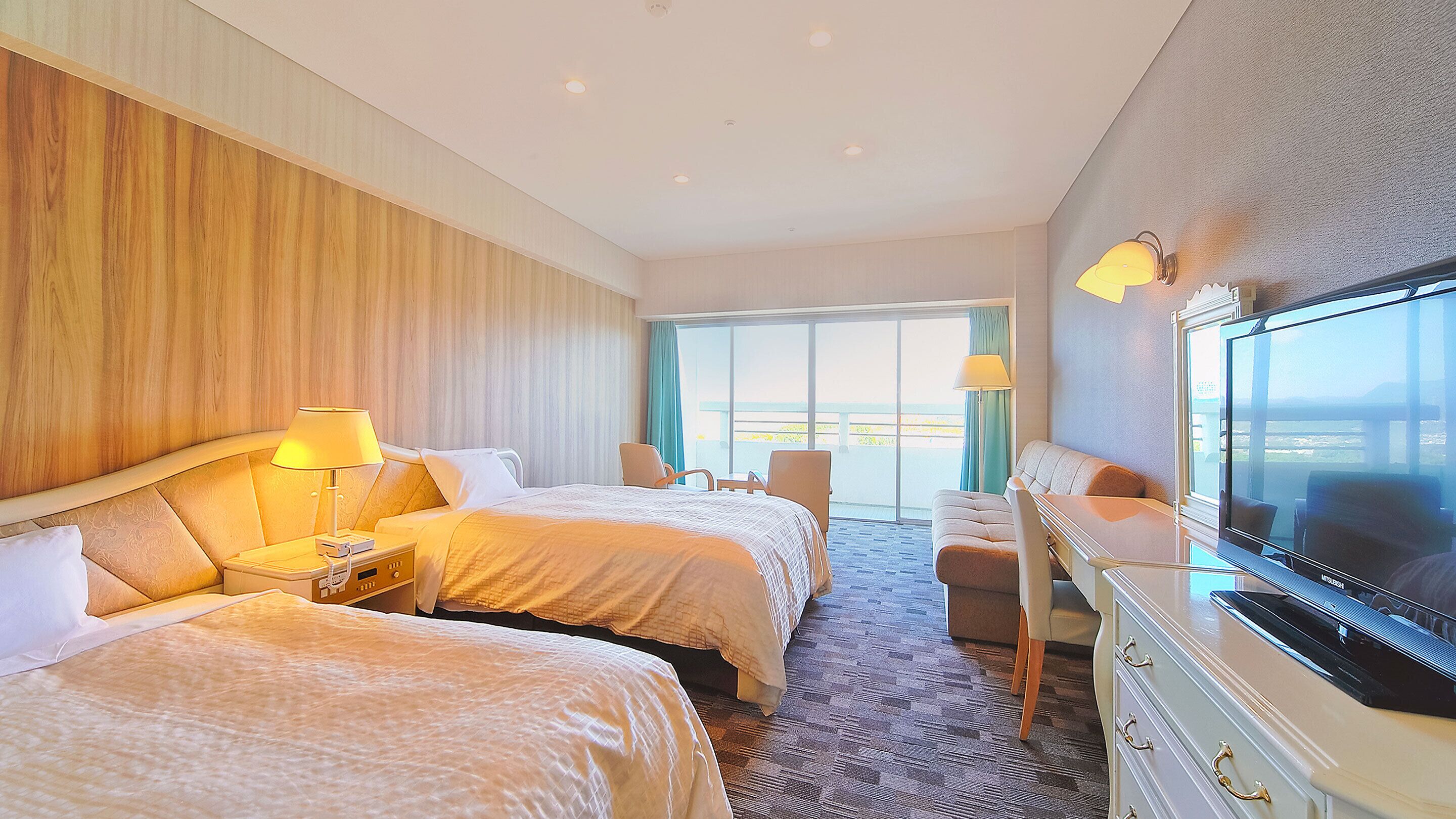 A hotel room with two beds, a TV, a desk, and a balcony with a view.