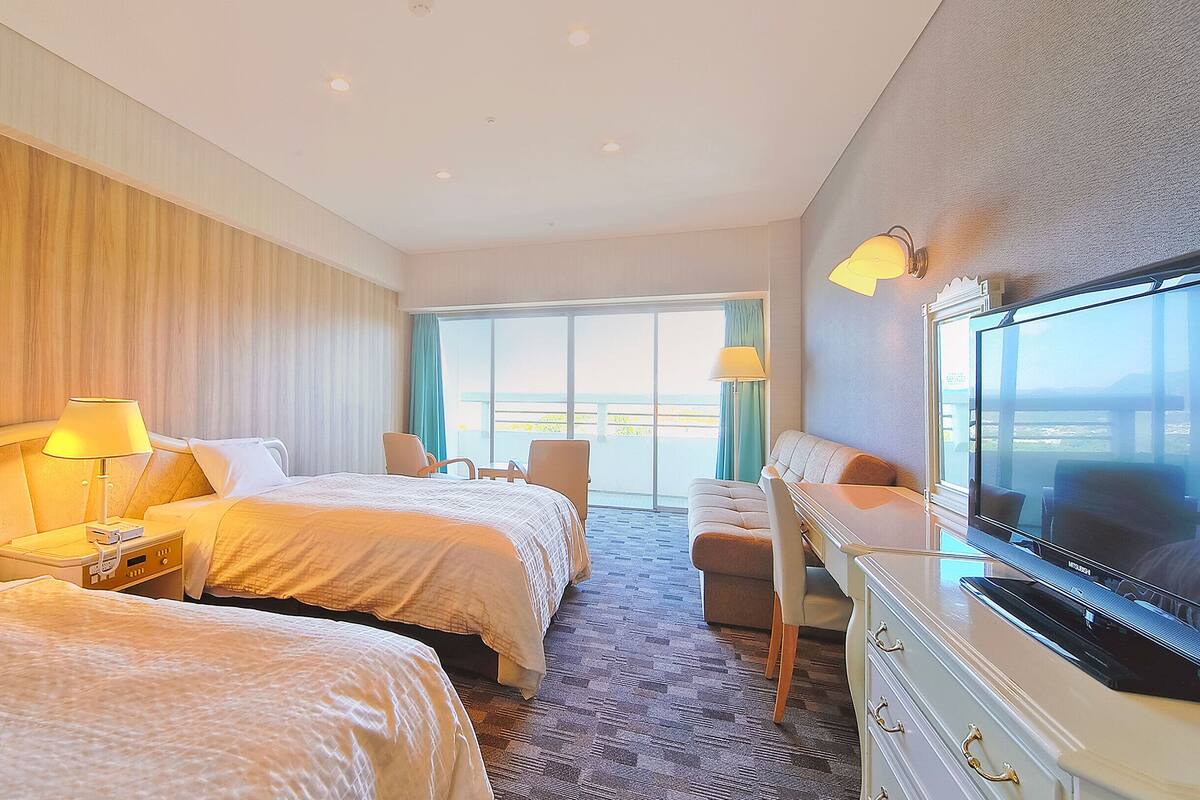 Une chambre d’hôtel avec deux lits, une télévision et un balcon offrant une vue.