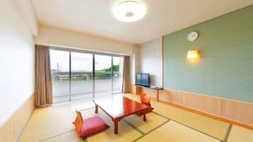 A hotel room with tatami flooring, a sliding glass door to a balcony, a wooden table, a TV, and a clock on the wall.