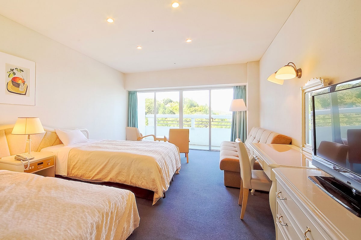 A hotel room with two beds, a desk, a chair, a television, and a window with a view.