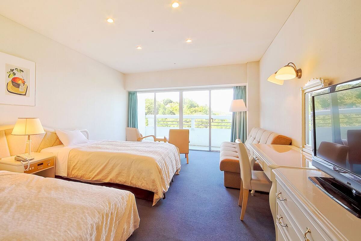 Une chambre d’hôtel avec deux lits, un bureau, une chaise, une télévision et un balcon avec vue.