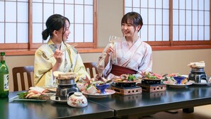 Two people in traditional attire at a table with various dishes, chopsticks, and a bottle. - Ikoi no Mura Noto Hanto (Shika)