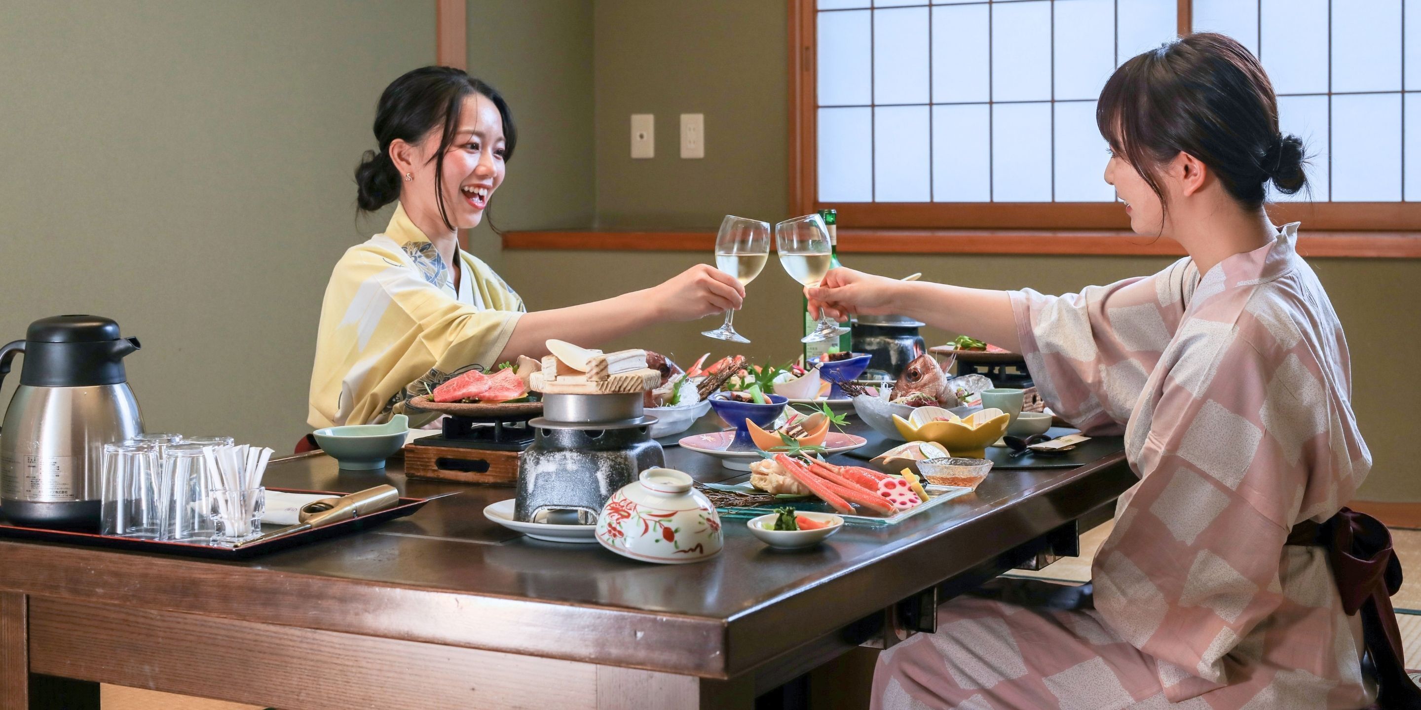 Ein traditioneller japanischer Esstisch mit Holztisch, verschiedenen Gerichten und zwei Personen, die mit Gläsern anstoßen.