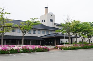 A modern building with a central tower, surrounded by a parking lot and flower beds. - Ikoi no Mura Noto Hanto (Shika)