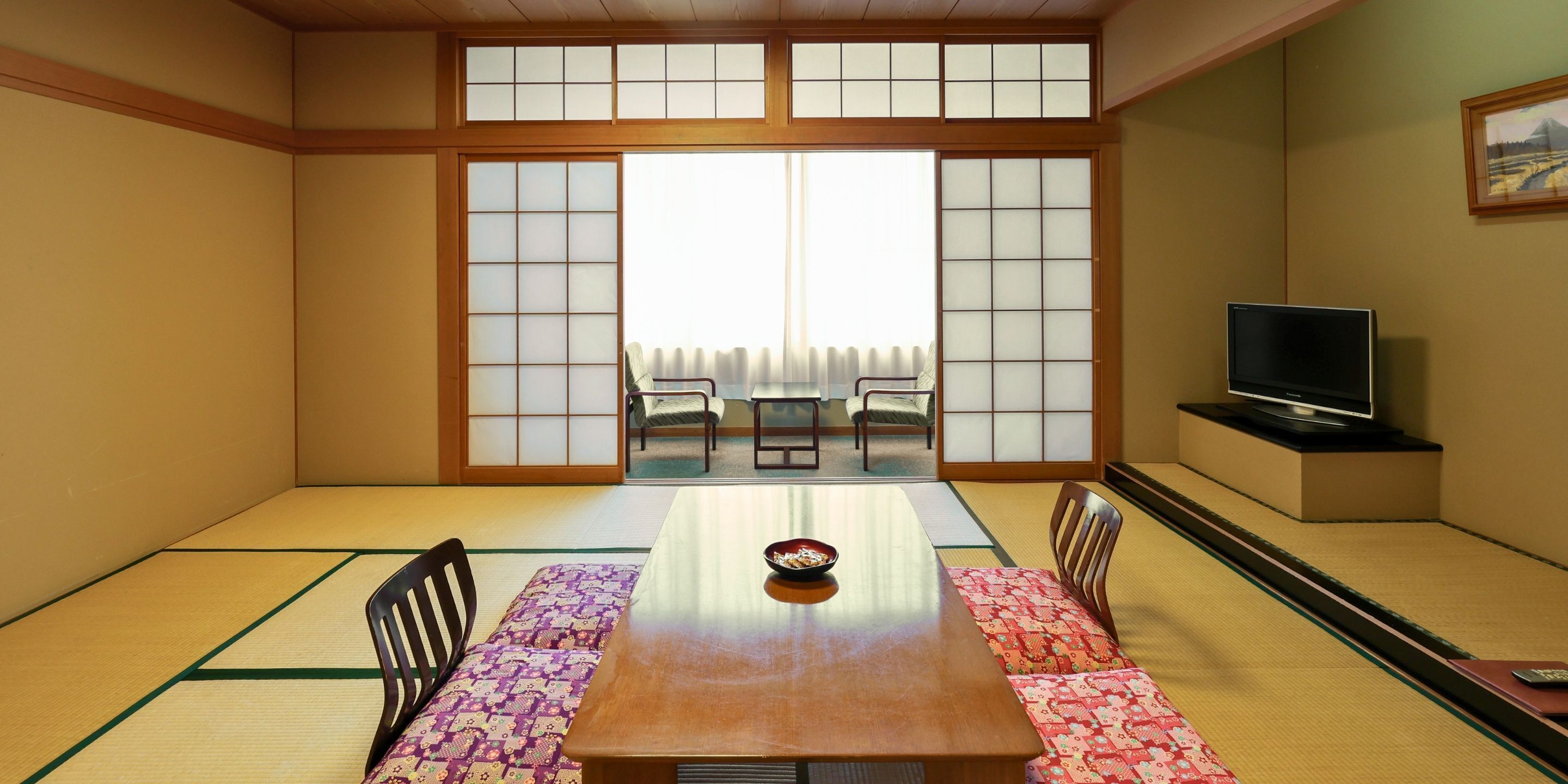 Et traditionelt japansk rum med tatamimåtter, et lavt bord og skydedøre, der fører til en balkon.