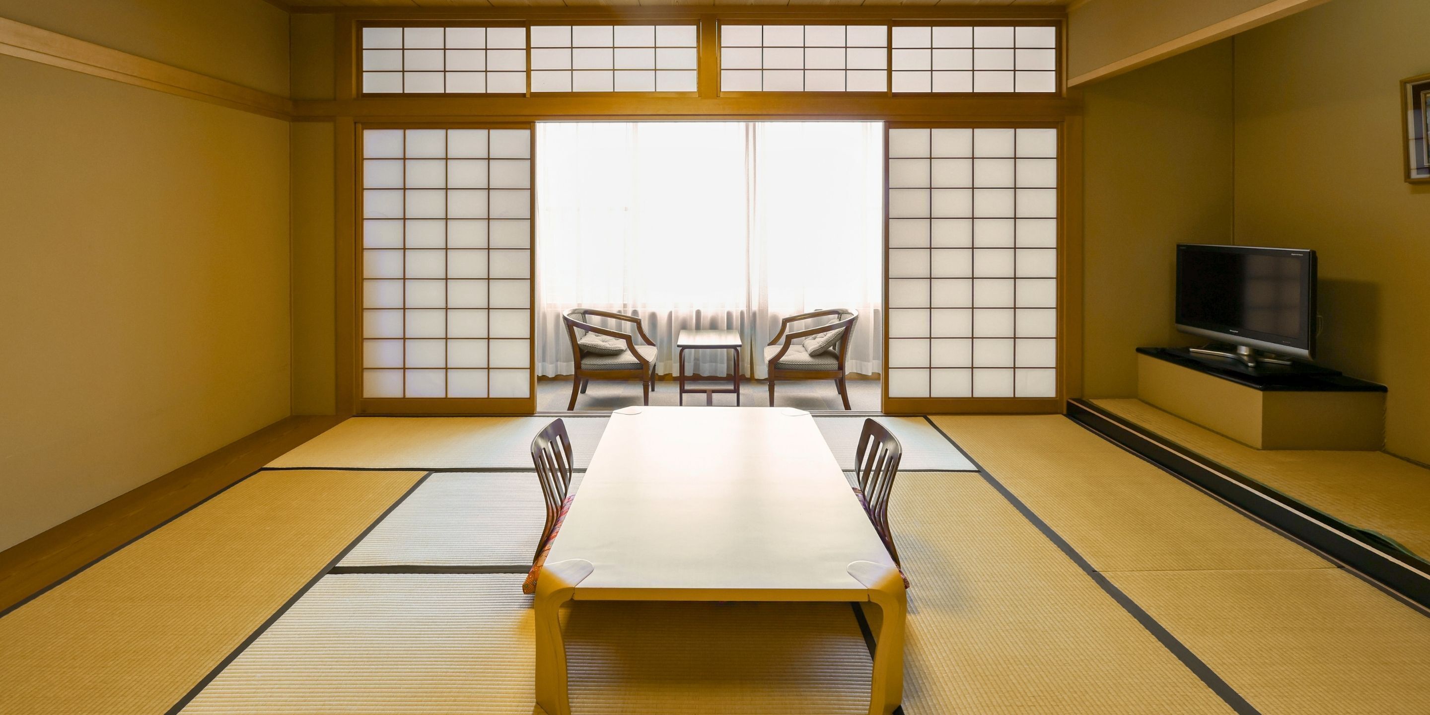 Una habitación tradicional japonesa con suelo de tatami, una mesa baja, dos sillas y un televisor sobre un mueble.