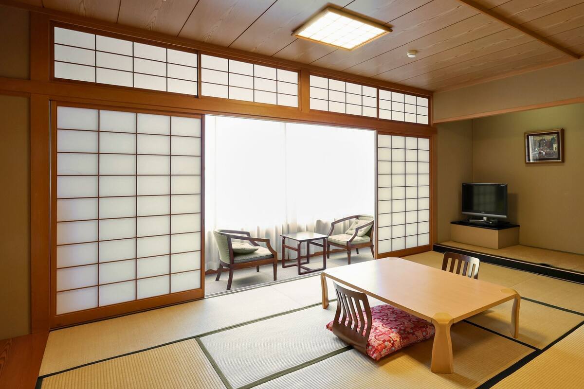 A traditional Japanese room with tatami flooring, a low table, chairs, a television, and sliding doors.