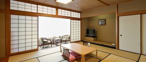 A traditional Japanese room with tatami flooring, a low table, chairs, a television, and sliding doors.