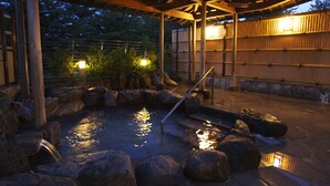 A traditional Japanese onsen with a wooden structure, hot spring bath surrounded by rocks, and a wooden fence. - Ikoi no Mura Noto Hanto (Shika)