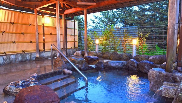 A traditional Japanese onsen with a wooden deck, stone steps, and a stone bath surrounded by rocks. - Ikoi no Mura Noto Hanto (Shika)