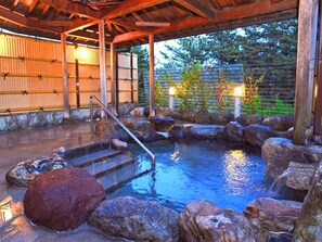 Een traditioneel Japans onsen met een houten terras, stenen trappen en een stenen bad omringd door rotsen.
