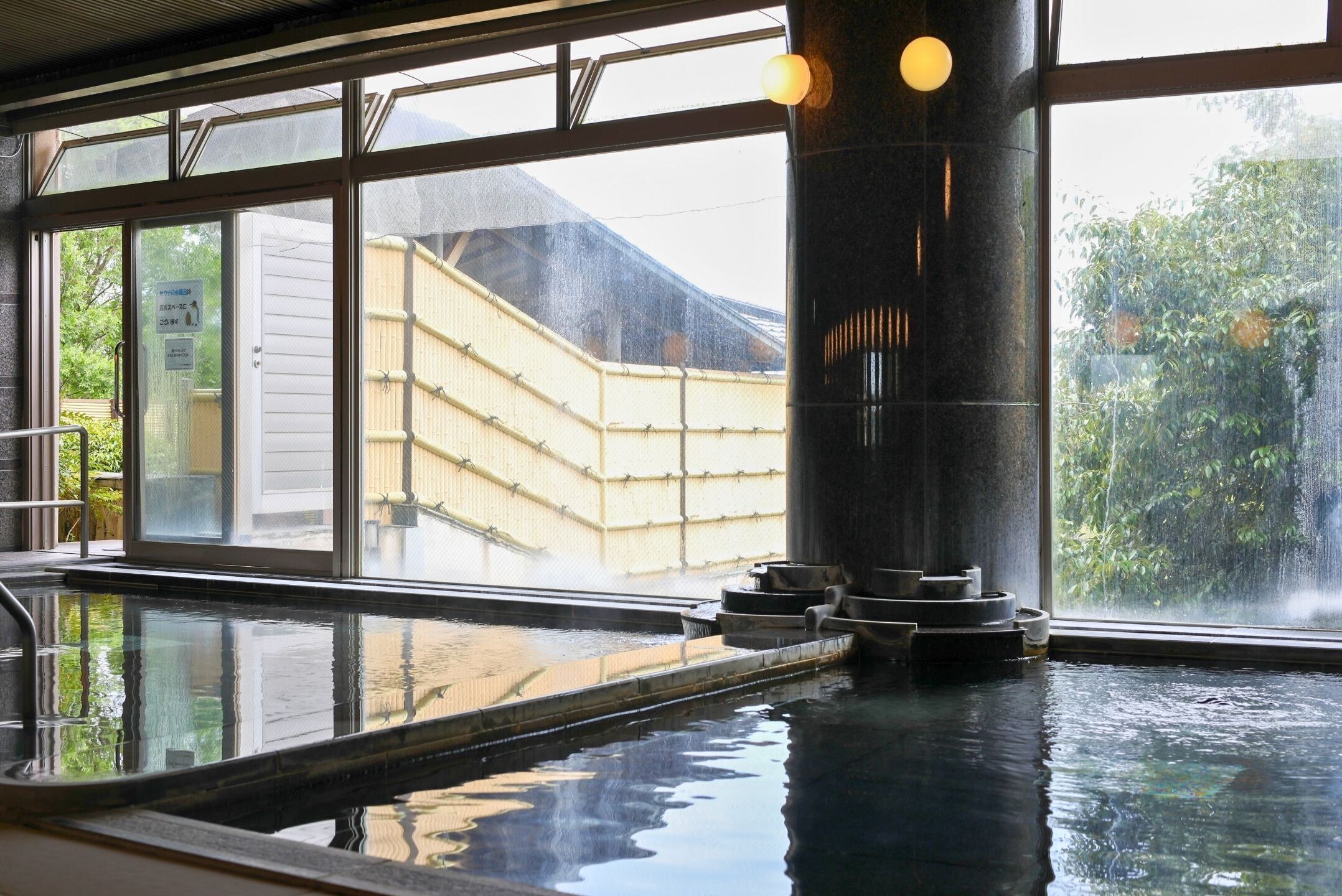 A traditional Japanese onsen with a view of a bamboo fence and a wooden building outside.