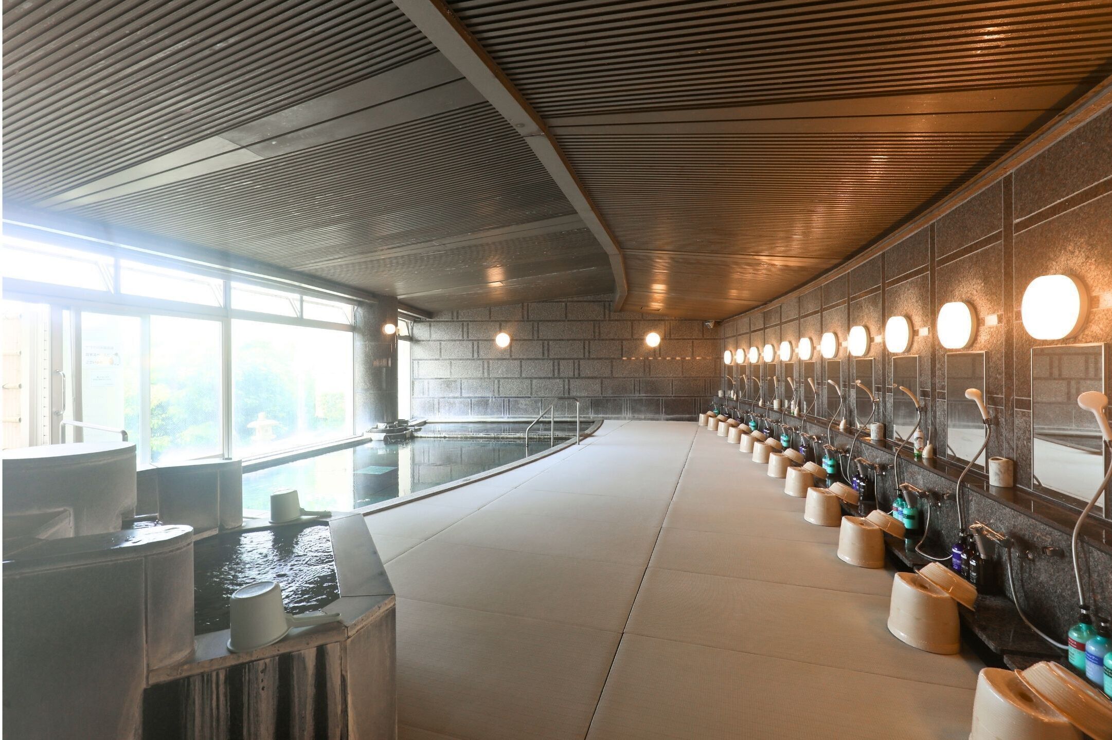 A long, modern bathroom with a central pool, multiple sinks, and a row of round mirrors.