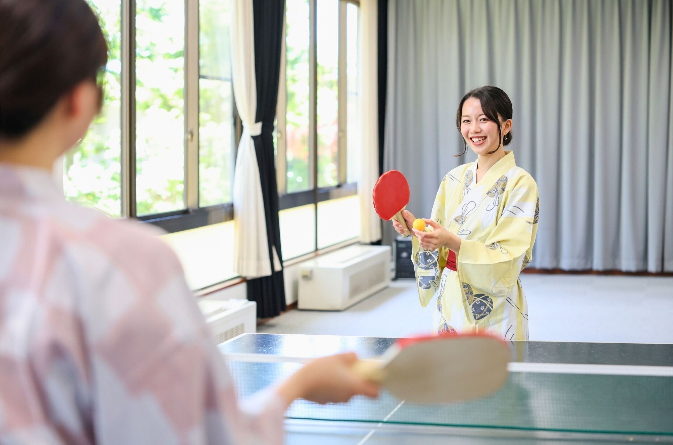 A room with a ping pong table, a person in traditional attire, and a window with curtains.