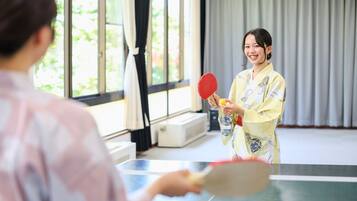 A room with a ping pong table, a person in traditional attire, and a window with curtains.