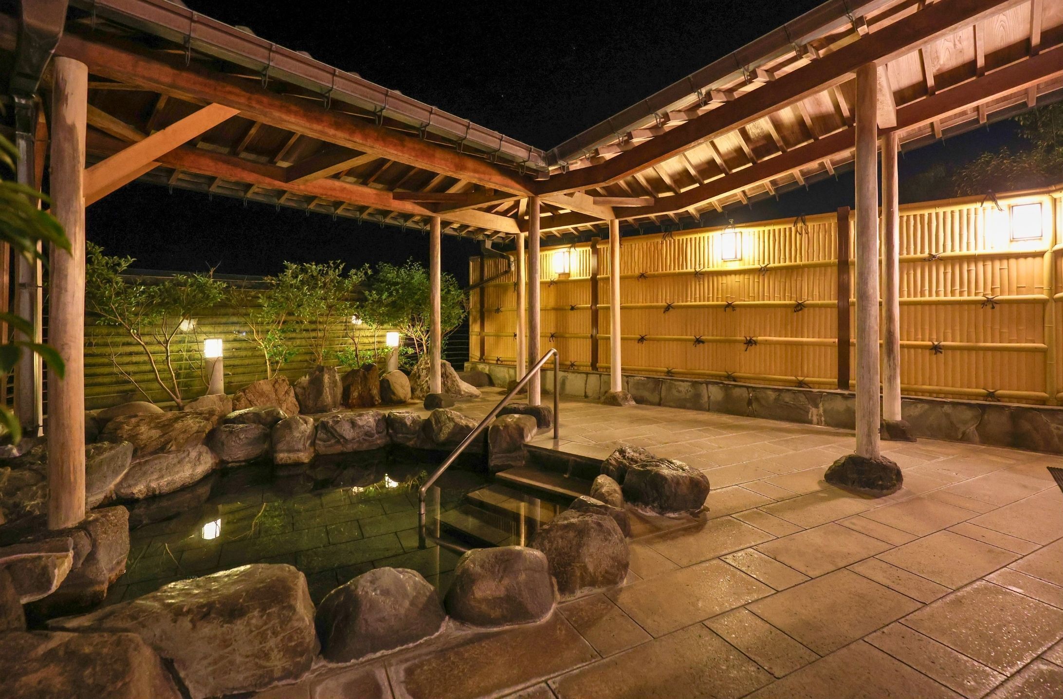 Un onsen japonais traditionnel, avec un bain en pierre, des piliers en bois et un sol carrelé.