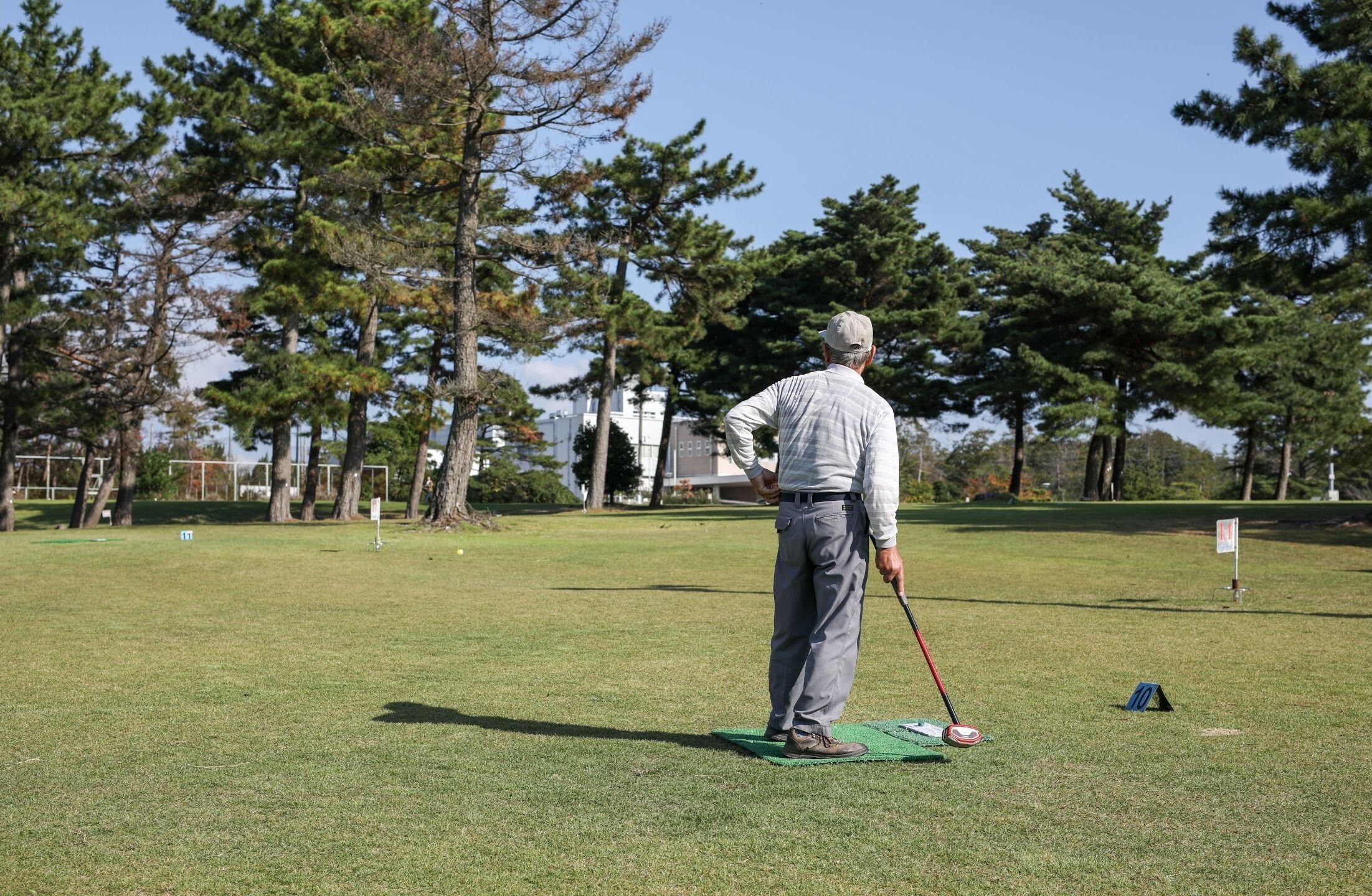 A man on a golf course with trees and buildings in the background.