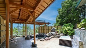 A covered outdoor area with a stone hot tub, rocks, and a wooden pergola. - Ikoi no Mura Noto Hanto (Shika)