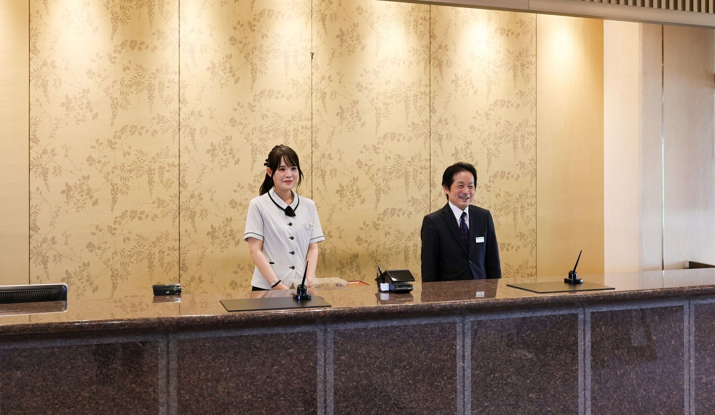 A reception desk with a floral wallpaper background, a nameplate, and a telephone.