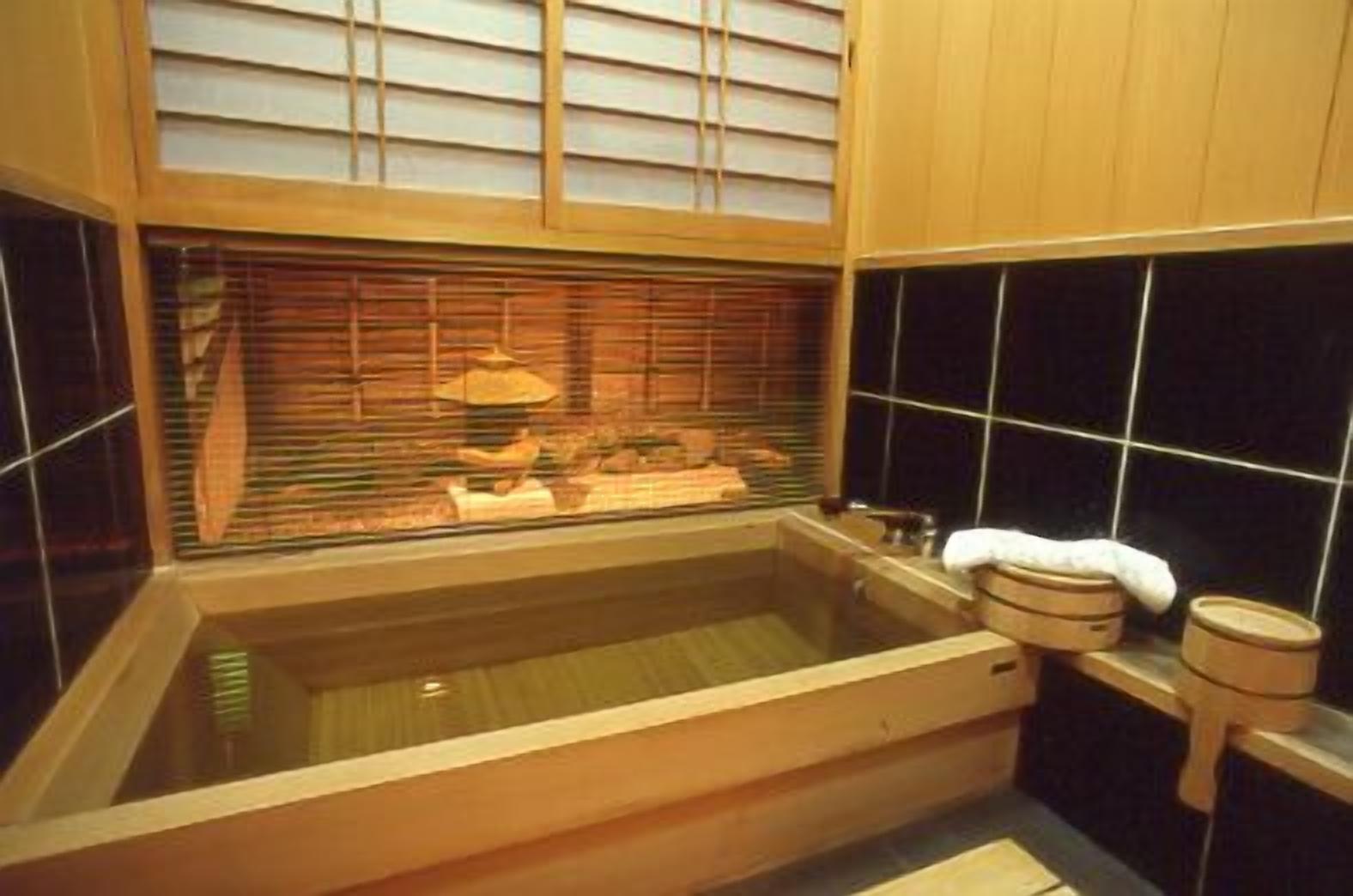 A traditional Japanese-style bath with a wooden tub, a window with blinds, and a tiled wall.