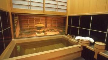 A traditional Japanese-style bath with a wooden tub, a window with blinds, and a tiled wall.
