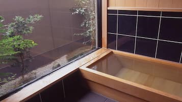 A corner of a room with a wooden bench, a black tiled wall, and a small plant.