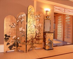 Una habitación japonesa tradicional con suelo de tatami, pantalla shoji y un panel decorativo de madera con motivos florales.