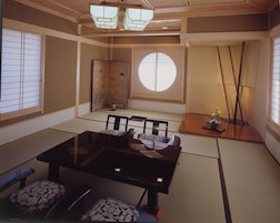 Una habitación japonesa tradicional con suelo de tatami, una mesa baja con cojines y puertas correderas.