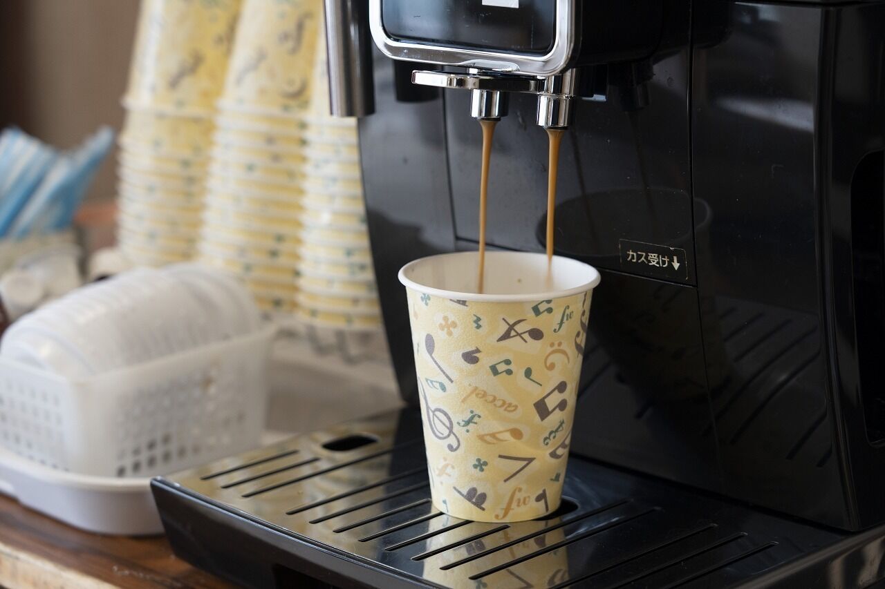 Una máquina de café vertiendo café en una taza con notas y símbolos musicales.
