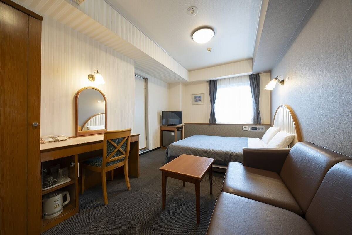 A hotel room with a bed, a desk, a chair, a small table, a television, and a mirror.