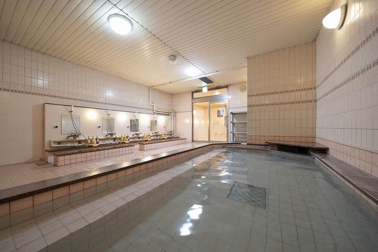 Un área de baños públicos con múltiples lavamanos, una piscina central grande y suelo de baldosas.