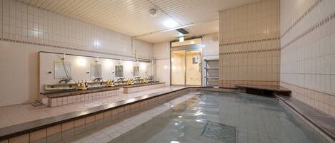 Un área de baños públicos con múltiples lavamanos, una piscina central grande y suelo de baldosas.