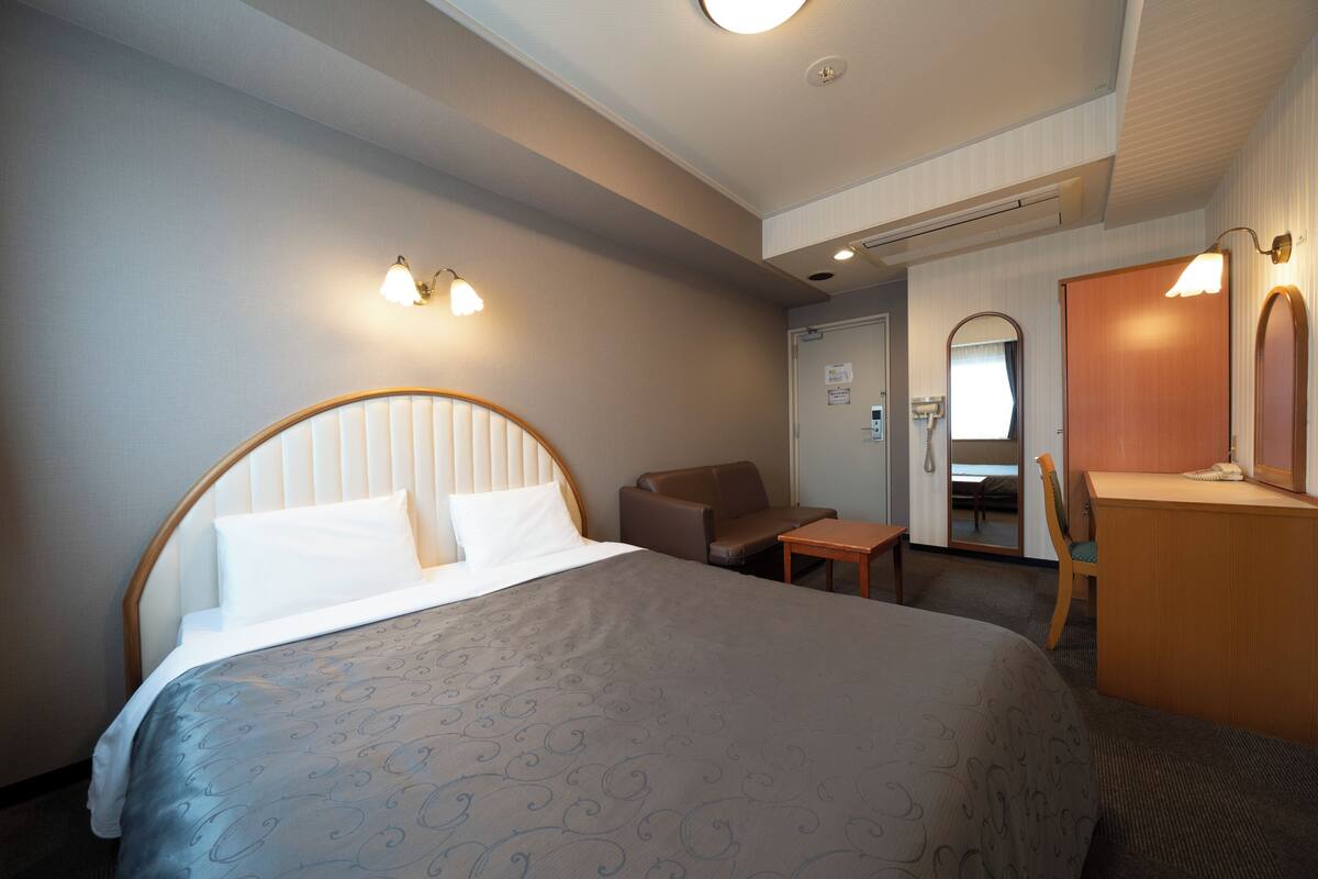 A hotel room with a large bed, a desk, a chair, and a mirror.