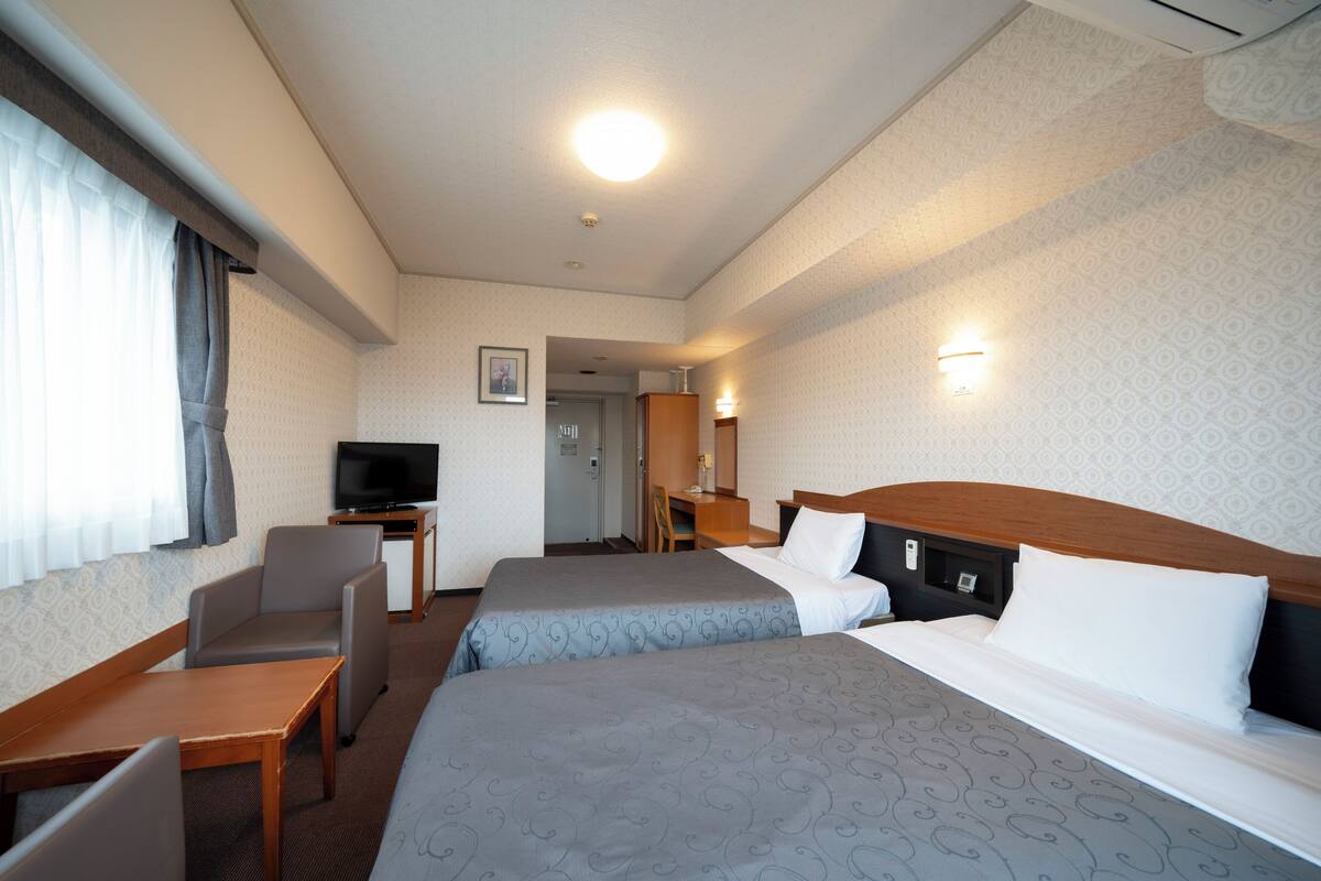 A hotel room with two beds, a desk, a chair, a television, and a bathroom visible through an open door.