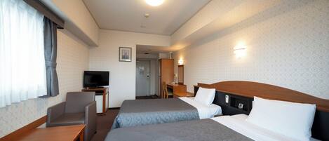 A hotel room with two beds, a desk, a chair, a television, and a bathroom visible through an open door.