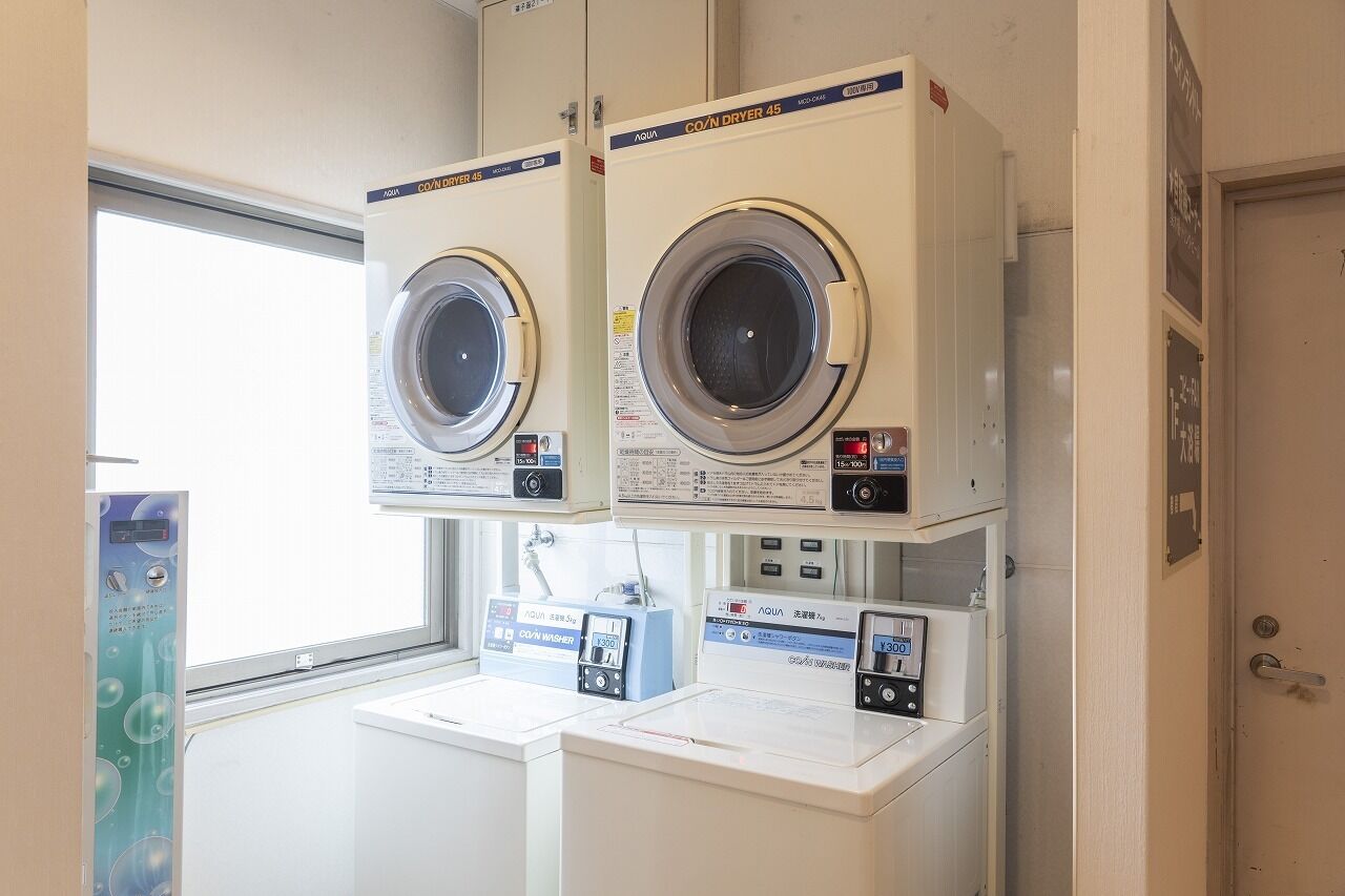 Een wasserette met twee voorladers wasmachines en drogers, een bedieningspaneel en een raam.